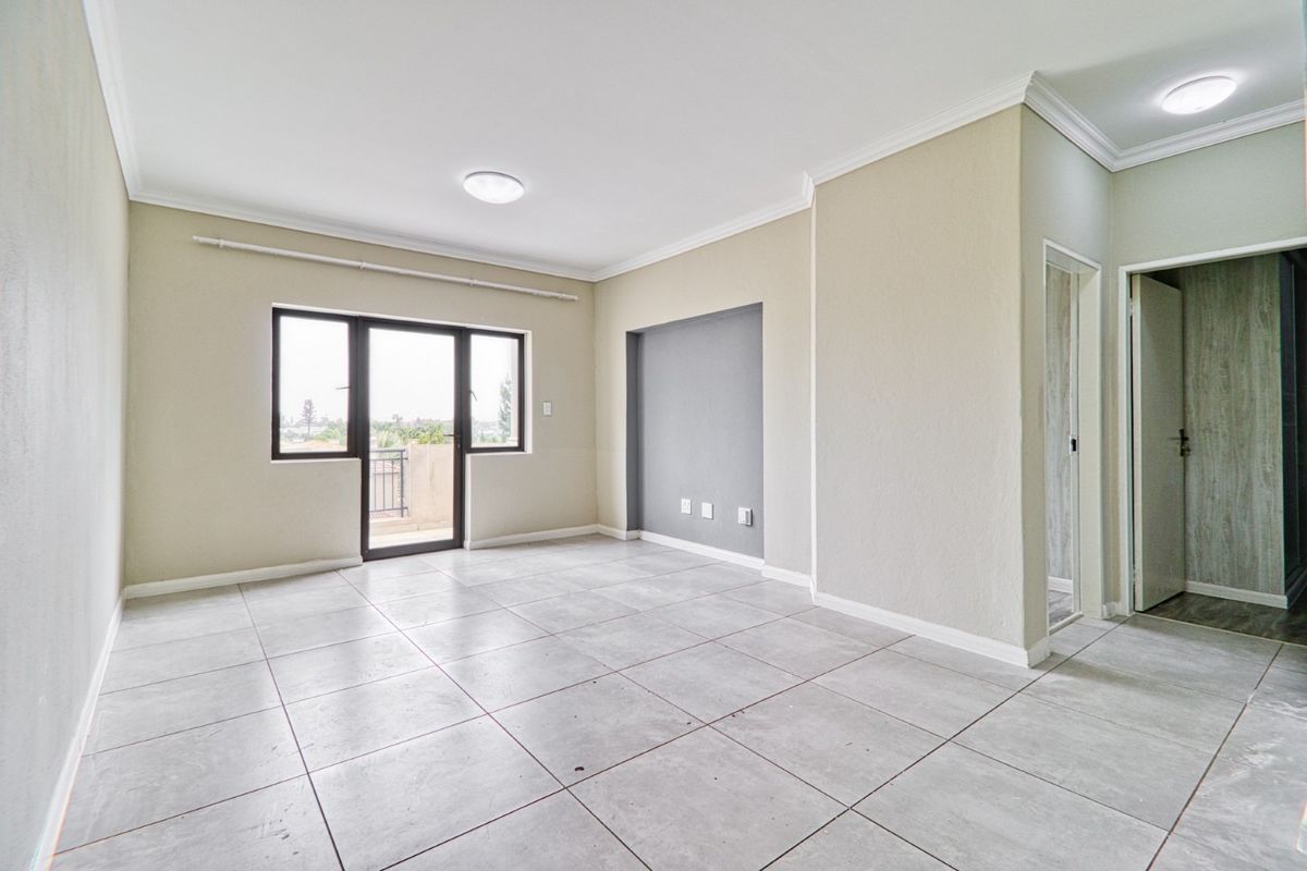 A bright, open-plan living area featuring neutral tiled flooring, a recessed feature wall, and direct access to a private balcony.