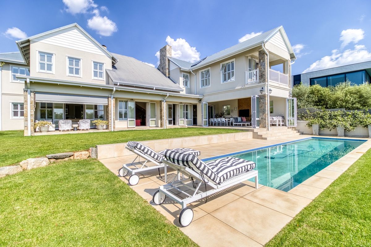 A beautifully maintained rear exterior featuring a swimming pool, stone-clad accents, a covered patio area, and a spacious lawn.