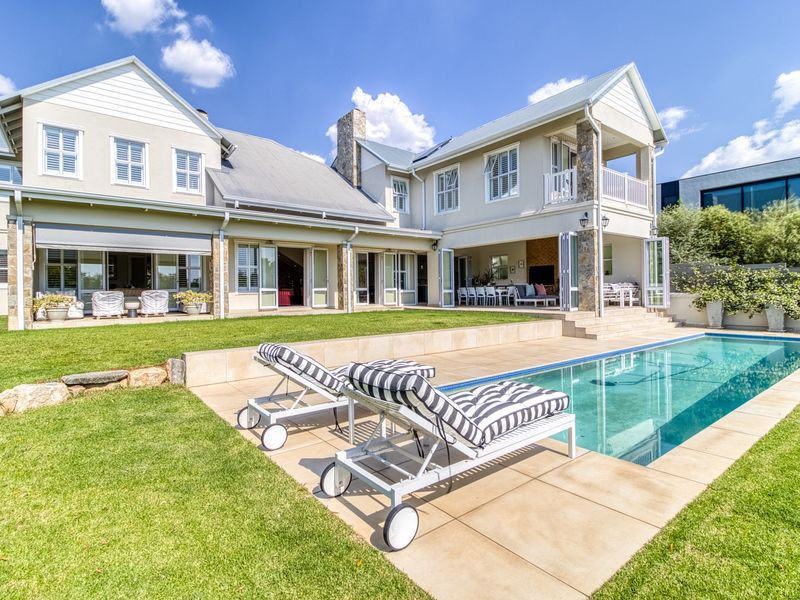 A beautifully maintained rear exterior featuring a swimming pool, stone-clad accents, a covered patio area, and a spacious lawn.