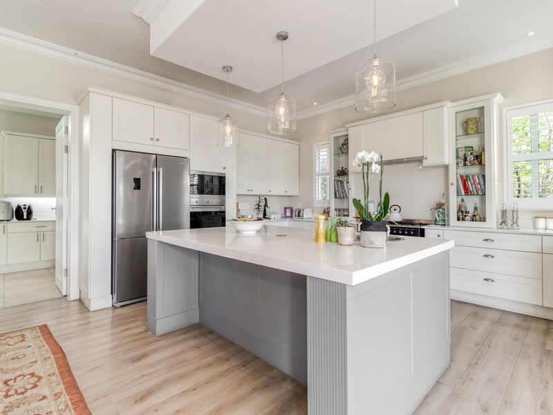 Modern kitchen featuring a central island with quartz countertops, white cabinetry, glass-front display units, and high-quality built-in appliances.
