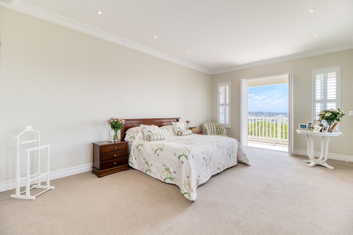 Spacious bedroom featuring neutral carpeting, crown molding, recessed lighting, and plantation shutters, with direct access to a private balcony offering scenic views.