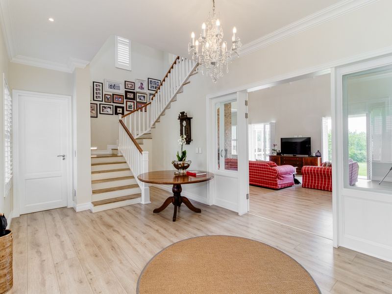 Spacious and bright entrance hall featuring timber flooring, a classic staircase with timber balustrade, and elegant glass-panelled doors leading to the living area.