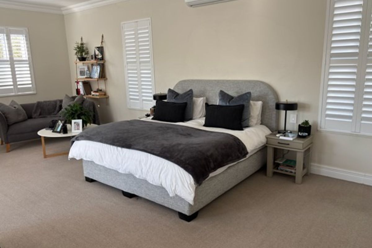 Spacious bedroom featuring neutral carpeting, plantation shutters, and a wall-mounted air conditioning unit.