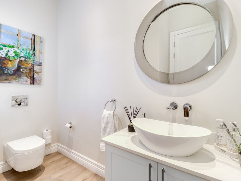 Modern bathroom featuring a wall-mounted toilet, a sleek vanity with a vessel sink, and a contemporary round mirror.