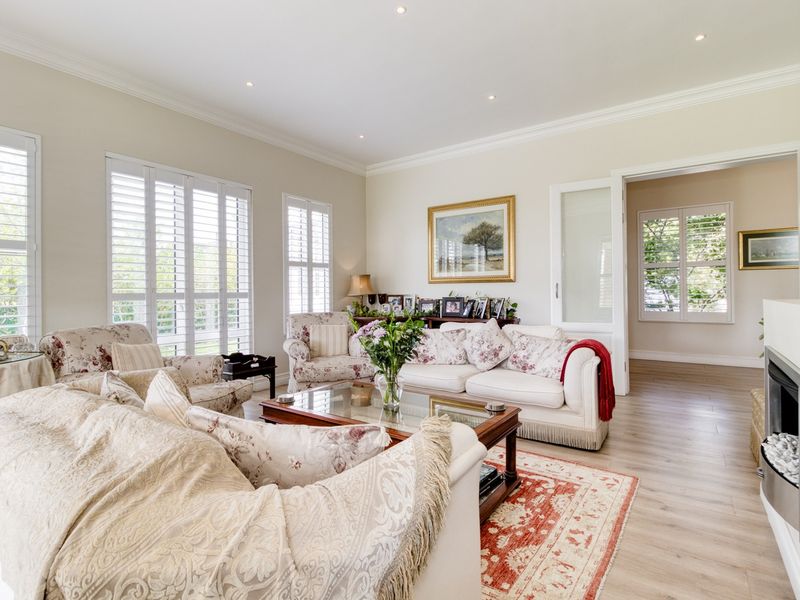 A bright and well-maintained living room featuring laminate flooring, recessed downlights, crown molding, and plantation shutters, with a built-in fireplace as a focal point.