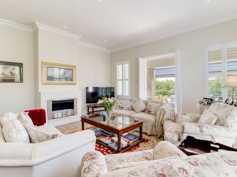 A bright and well-maintained living room featuring a built-in fireplace, crown molding, and plantation shutters with direct access to an outdoor patio area.
