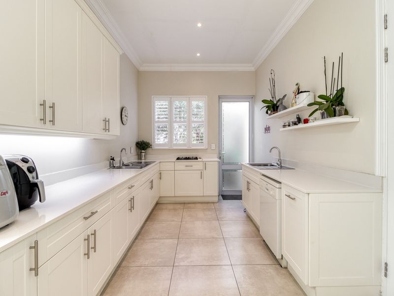 Modern galley-style kitchen featuring white cabinetry, stone countertops, integrated appliances, gas hob, and tiled flooring with ample natural light.