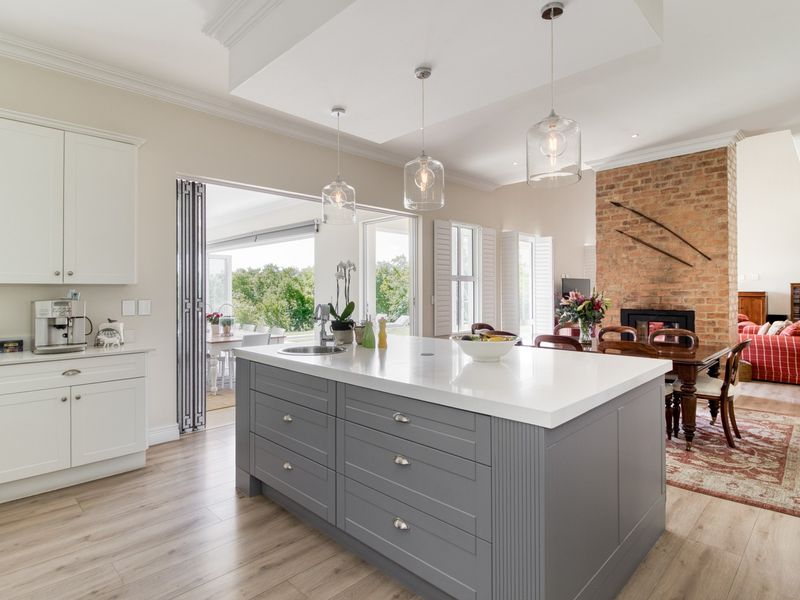 Spacious open-plan kitchen and living area featuring a large central island, modern cabinetry, exposed brick fireplace, and seamless access to the outdoor patio.
