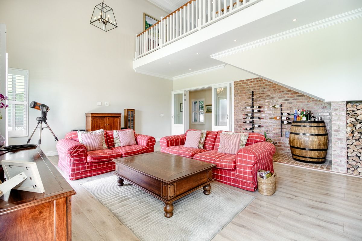 Spacious living room featuring a double-volume ceiling, mezzanine level, exposed brick feature wall, and light-toned laminate flooring.