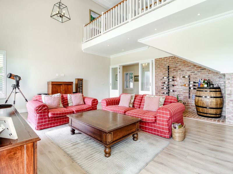 Spacious living room featuring a double-volume ceiling, mezzanine level, exposed brick feature wall, and light-toned laminate flooring.