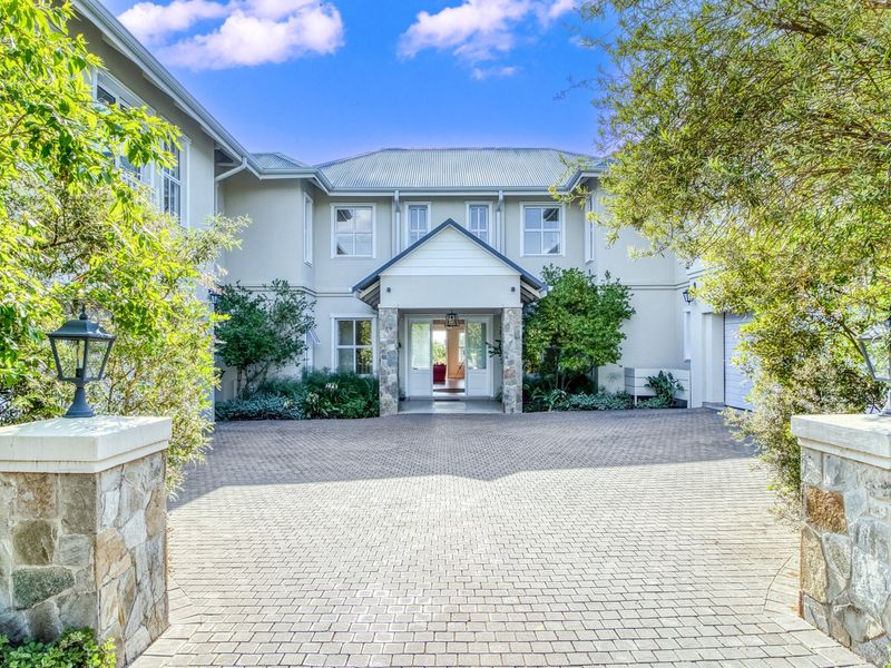 A well-maintained double-storey residence featuring a paved driveway, stone-clad entrance pillars, and a covered porch, presenting an inviting and elegant front facade.