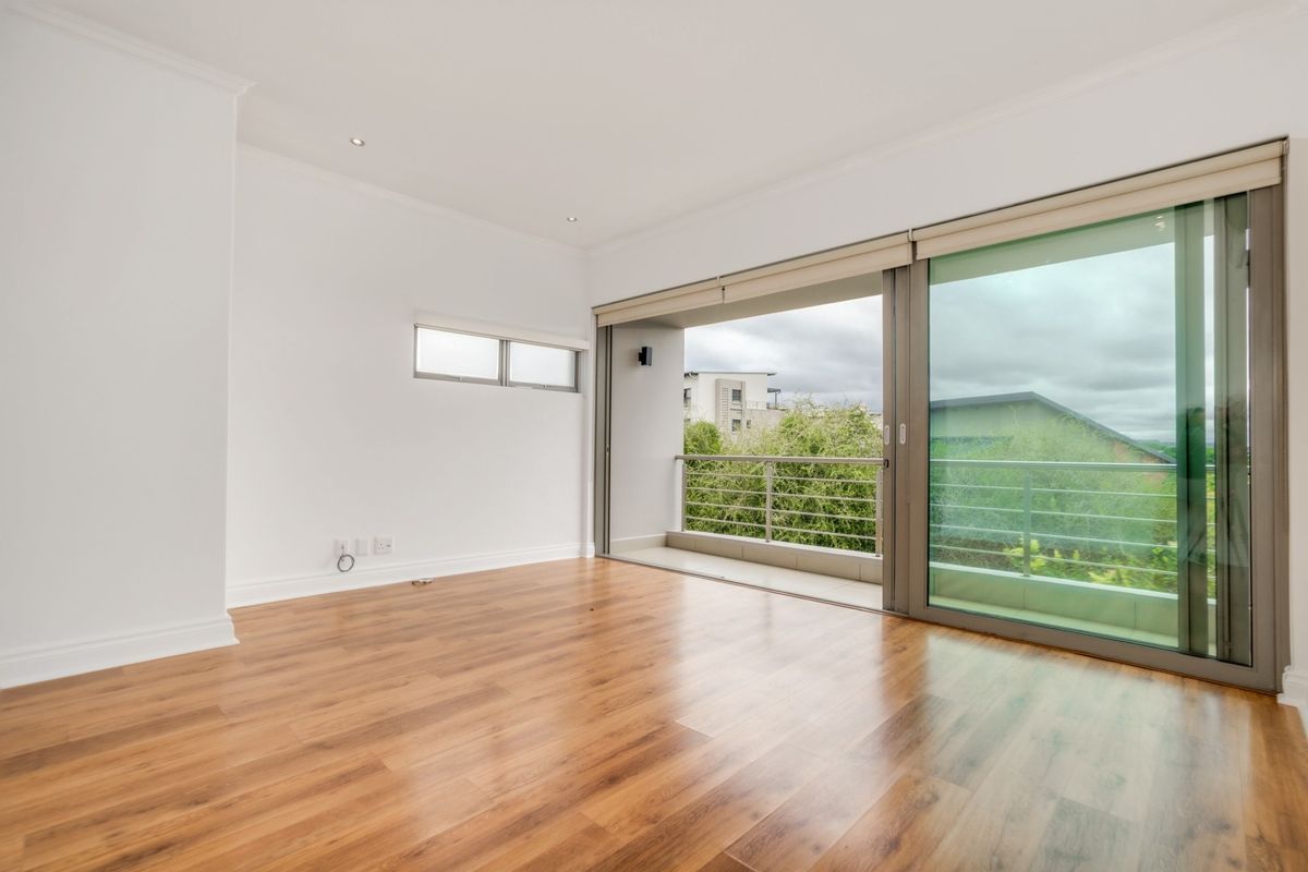 A bright, empty bedroom featuring wood-look laminate flooring, recessed ceiling lighting, and large sliding glass doors opening onto a private balcony.