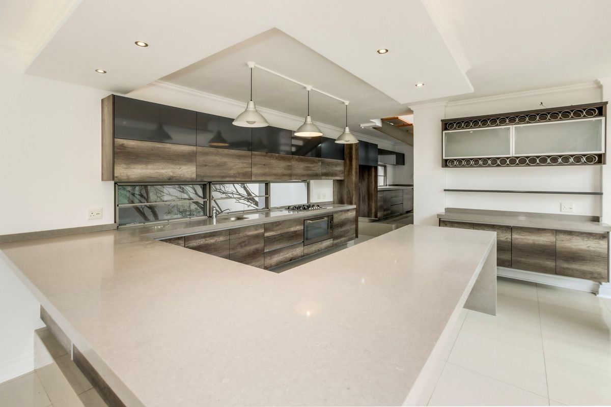 Modern kitchen featuring sleek wood-grain cabinetry, stone countertops, integrated oven and hob, and recessed ceiling lighting in an open-plan layout.