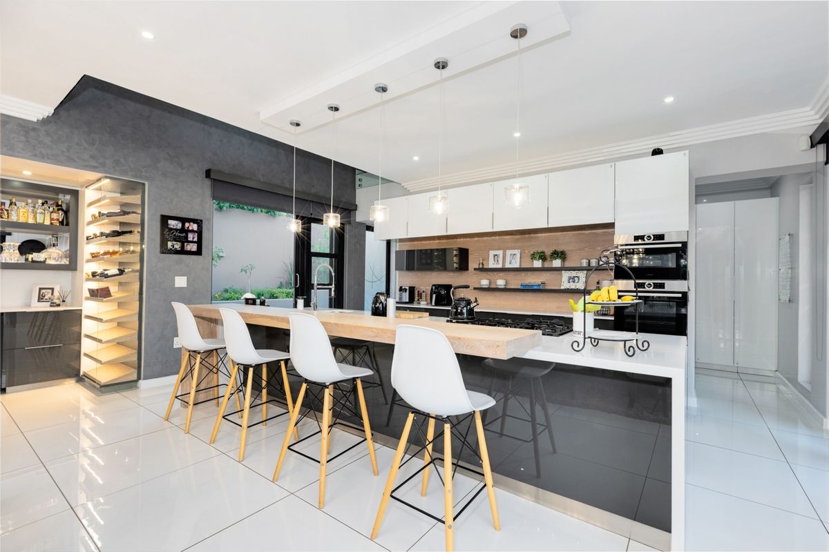 Modern kitchen featuring a large island with stone countertops, built-in appliances, integrated wine storage, and sleek cabinetry with contemporary pendant lighting.