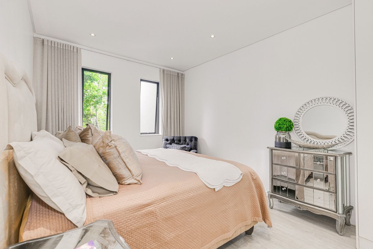 A bright and modern bedroom featuring neutral tones, recessed ceiling lighting, and large windows with floor-to-ceiling curtains.