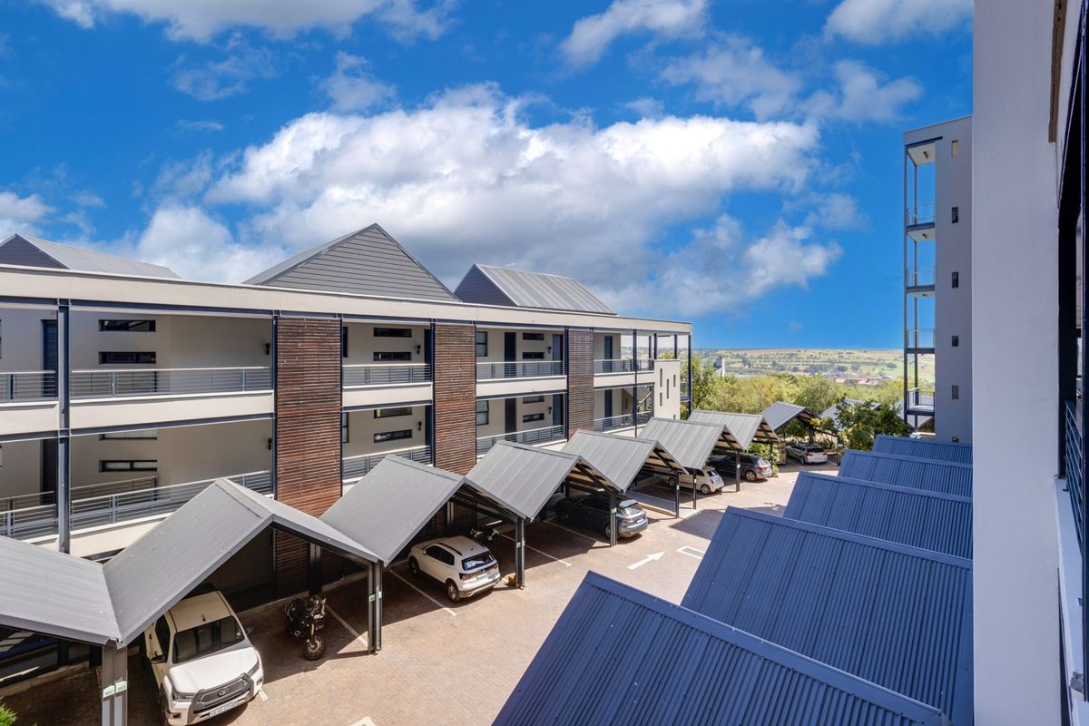 Elevated view of the apartment complex exterior, featuring covered parking bays and modern architectural design with timber cladding and metal roofing.