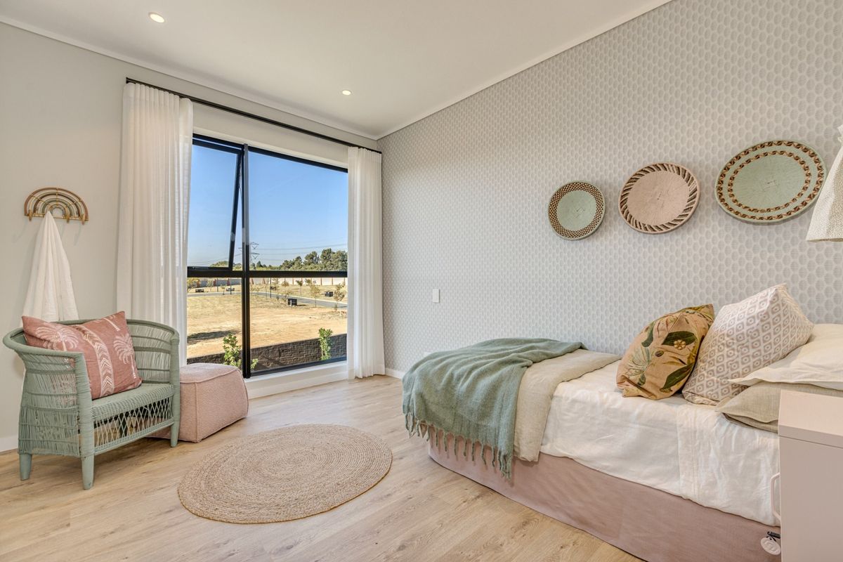 A bright and modern bedroom featuring light laminate flooring, textured wallpaper, and a large window providing natural light and exterior views.