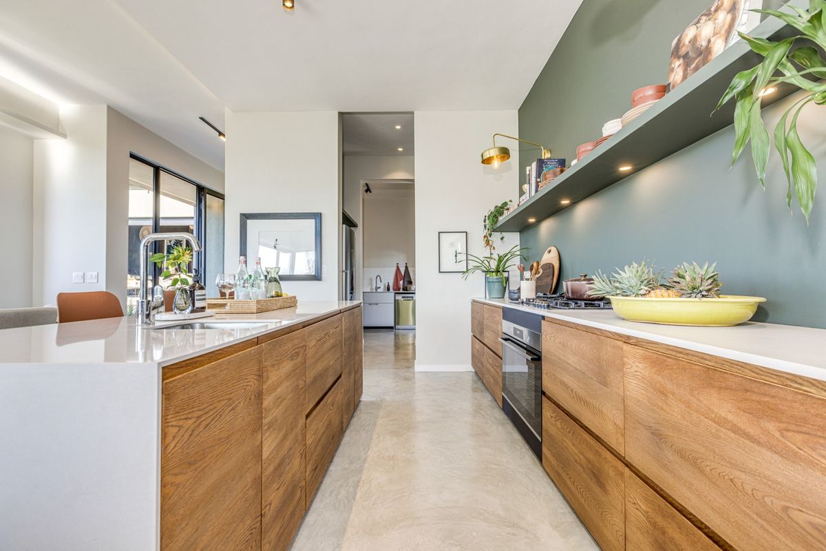Modern kitchen featuring timber cabinetry, stone countertops, a central island, and high-end built-in appliances, complemented by polished concrete floors and a feature wall.