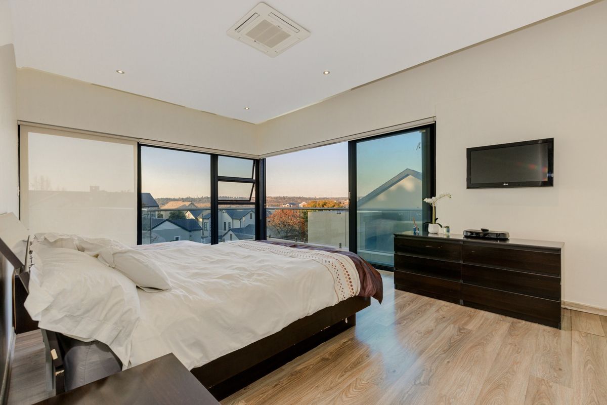 Spacious bedroom featuring floor-to-ceiling corner windows, integrated ceiling air conditioning, and access to a private balcony with scenic neighbourhood views.