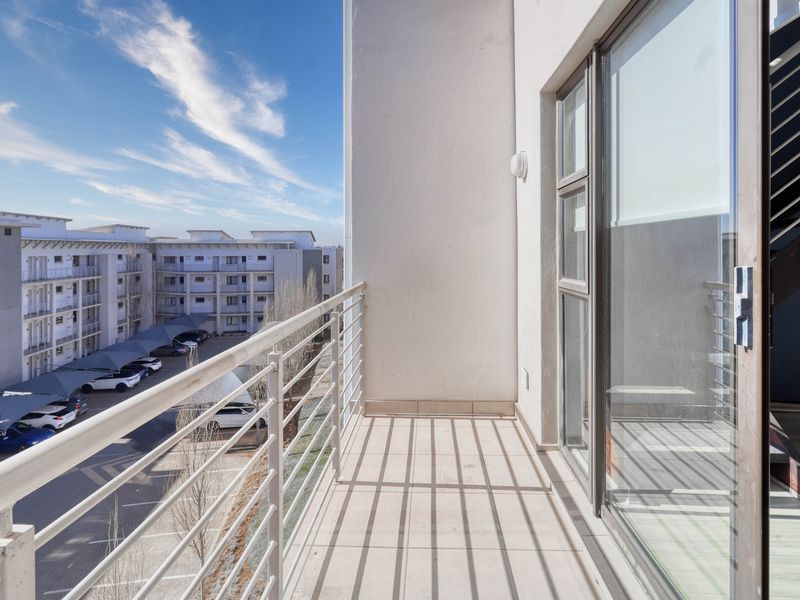 A clean, modern balcony with metal railings and tiled flooring, offering an elevated view of the complex parking area.
