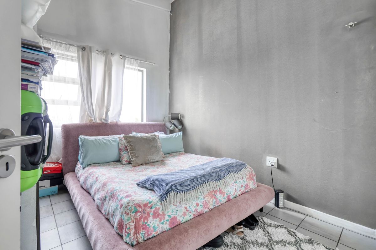 A compact bedroom featuring tiled flooring, a large window for natural light, and a neutral grey accent wall.