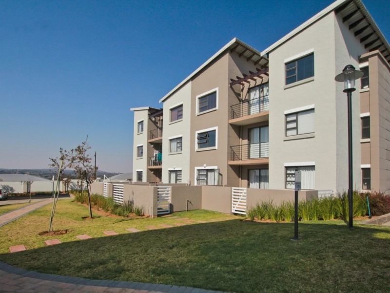 Exterior view of a modern multi-story apartment complex featuring balconies, paved walkways, and landscaped garden areas.
