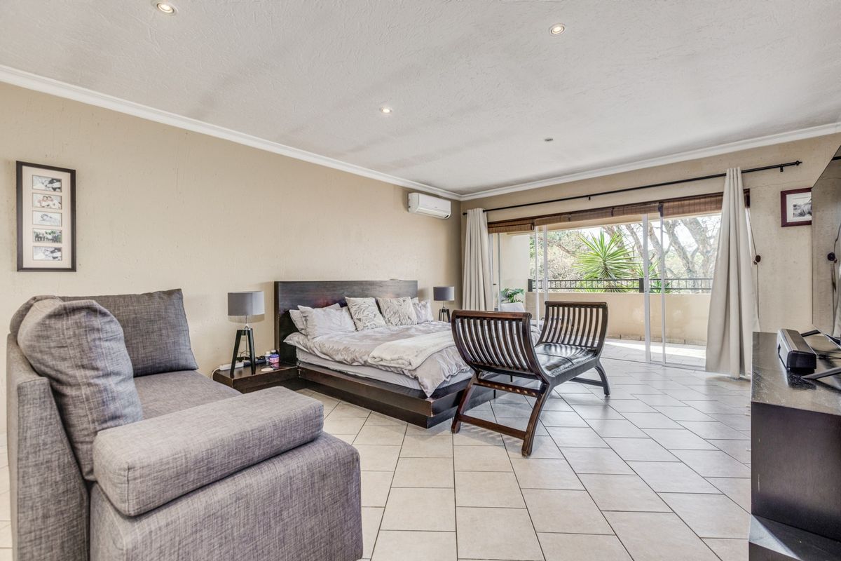Spacious bedroom featuring tiled flooring, recessed ceiling lighting, a wall-mounted air conditioning unit, and sliding glass doors leading to a private balcony.