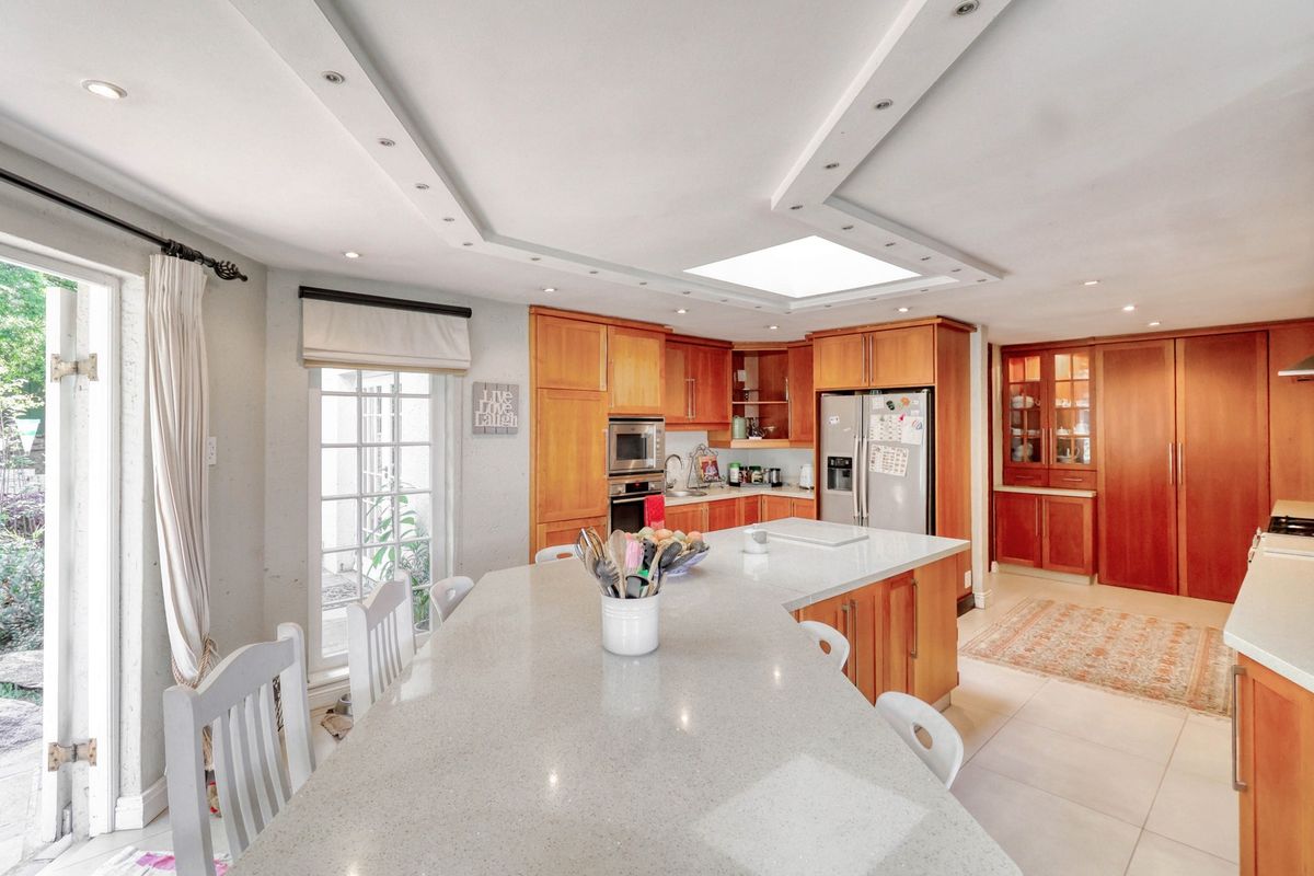 Spacious kitchen featuring warm wood cabinetry, a large central island with stone countertops, integrated appliances, and a skylight for natural illumination.