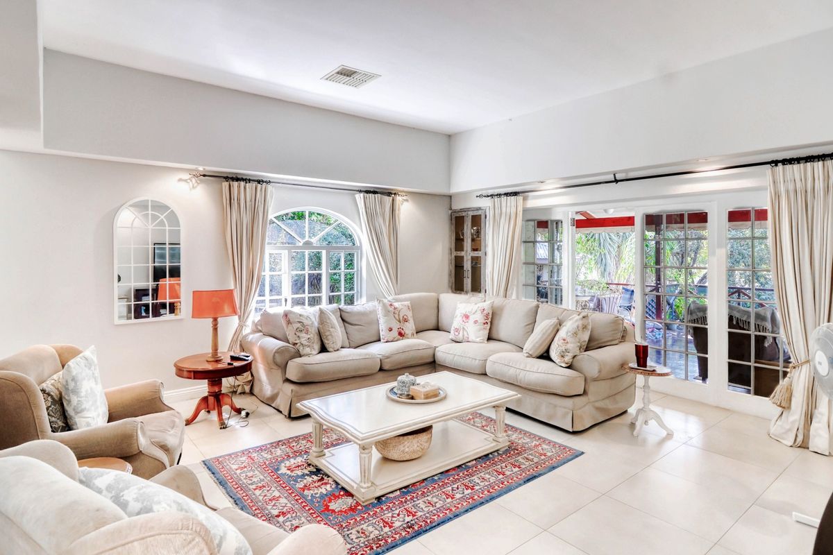 Spacious living room featuring large arched windows, tiled flooring, and sliding glass doors providing direct access to the outdoor patio area.