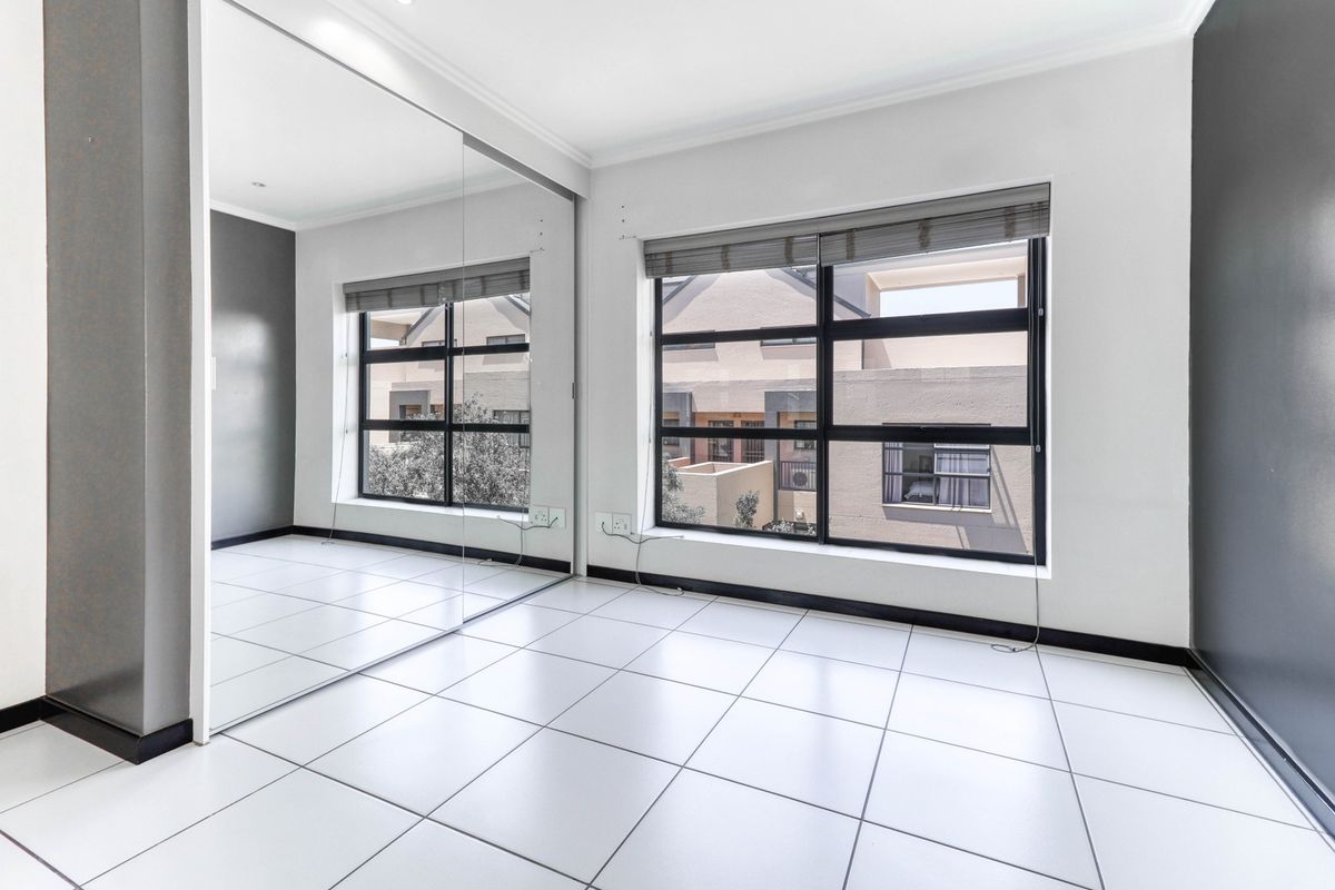 A bright, empty bedroom featuring large built-in mirrored wardrobes, modern tiled flooring, and aluminium-framed windows with venetian blinds.