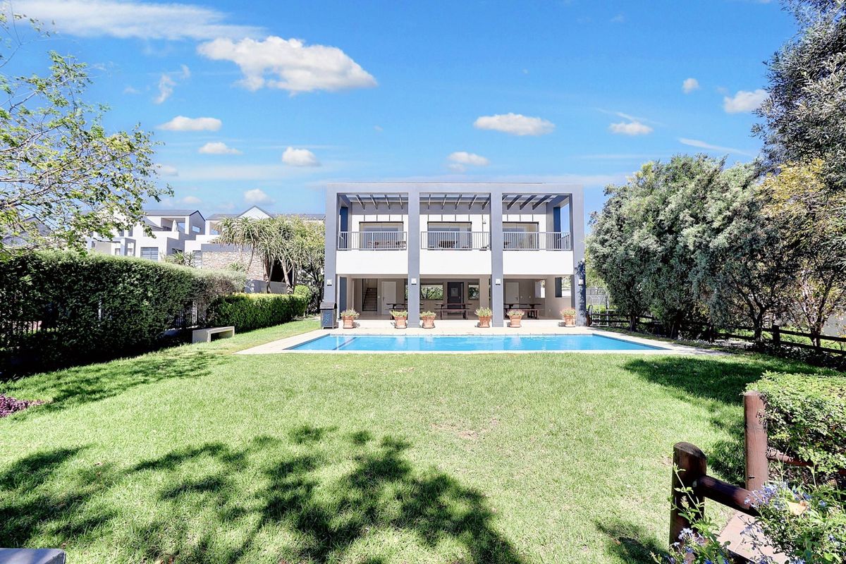 Rear view of the apartment building featuring a swimming pool, manicured lawn, and a covered patio area with an upper-level balcony.