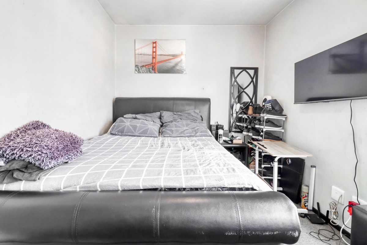 A compact bedroom featuring a wall-mounted television and neutral wall finishes, offering a functional space that could benefit from cosmetic updates.