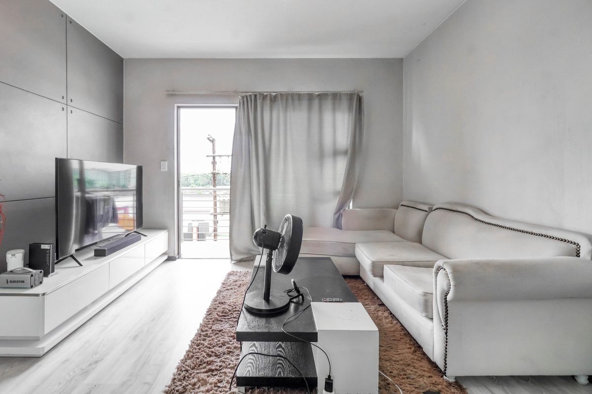 A bright living room featuring light laminate flooring, a built-in media console, and direct access to a balcony through a sliding glass door.