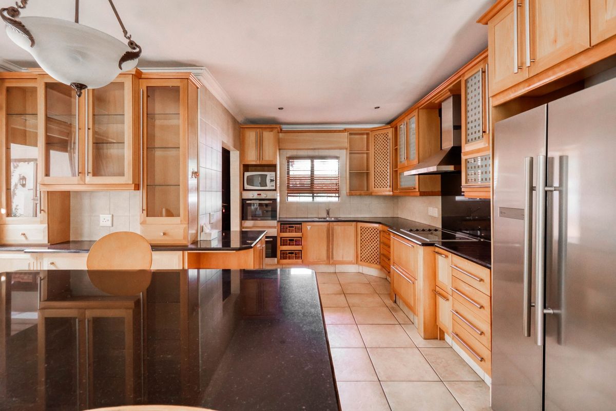 A functional kitchen featuring light wood cabinetry, dark granite countertops, a built-in oven, and a stainless steel extractor fan.