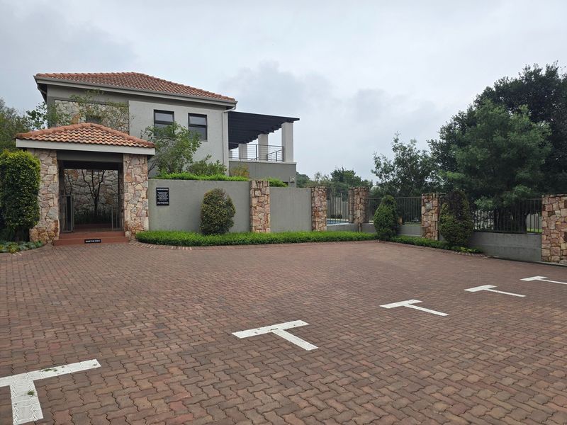 Front exterior view of the apartment complex featuring a paved parking area, stone-clad entrance, and well-maintained boundary walls.