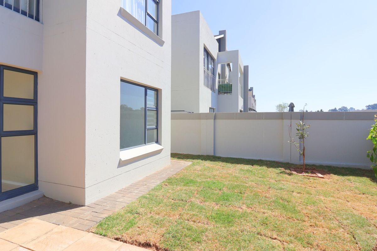 A view of the rear exterior of the apartment, featuring a small private garden, paved walkway, and modern boundary wall.