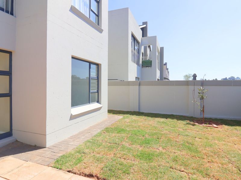 A view of the rear exterior of the apartment, featuring a small private garden, paved walkway, and modern boundary wall.