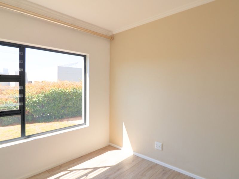 A bright, empty bedroom featuring neutral walls, laminate flooring, and a large window with an aluminium frame.