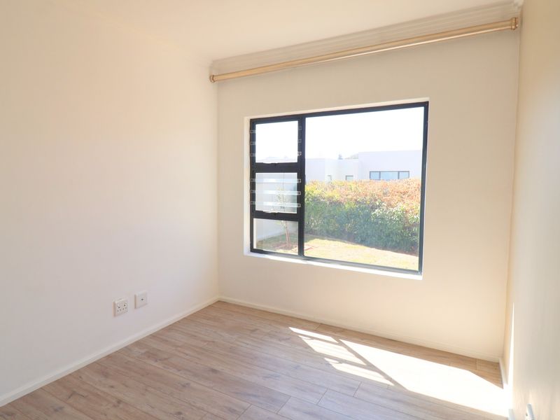 A bright, empty bedroom featuring modern laminate flooring, neutral walls, and a large window with an aluminium frame.