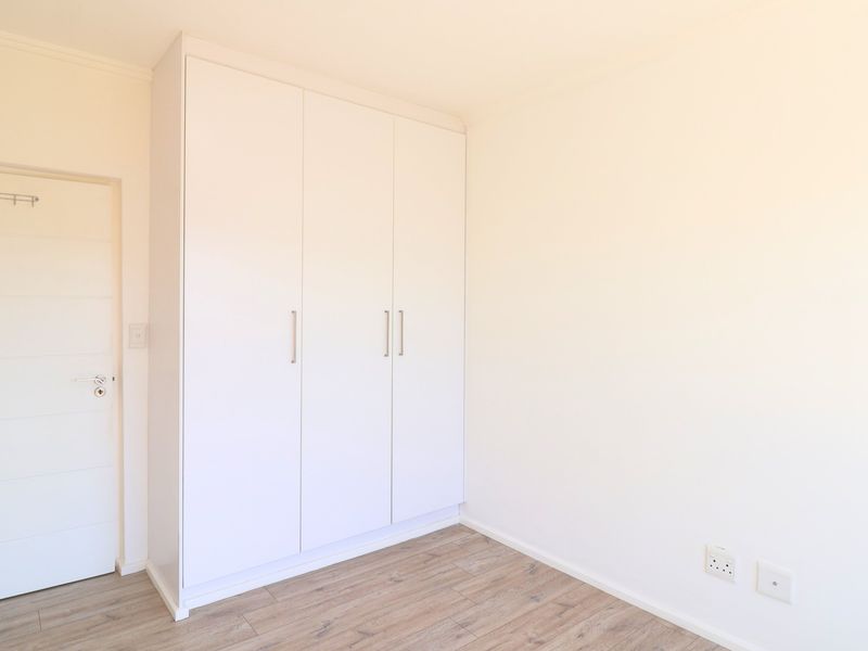 A bright, empty bedroom featuring modern laminate flooring, a clean white built-in wardrobe, and a neutral interior door.