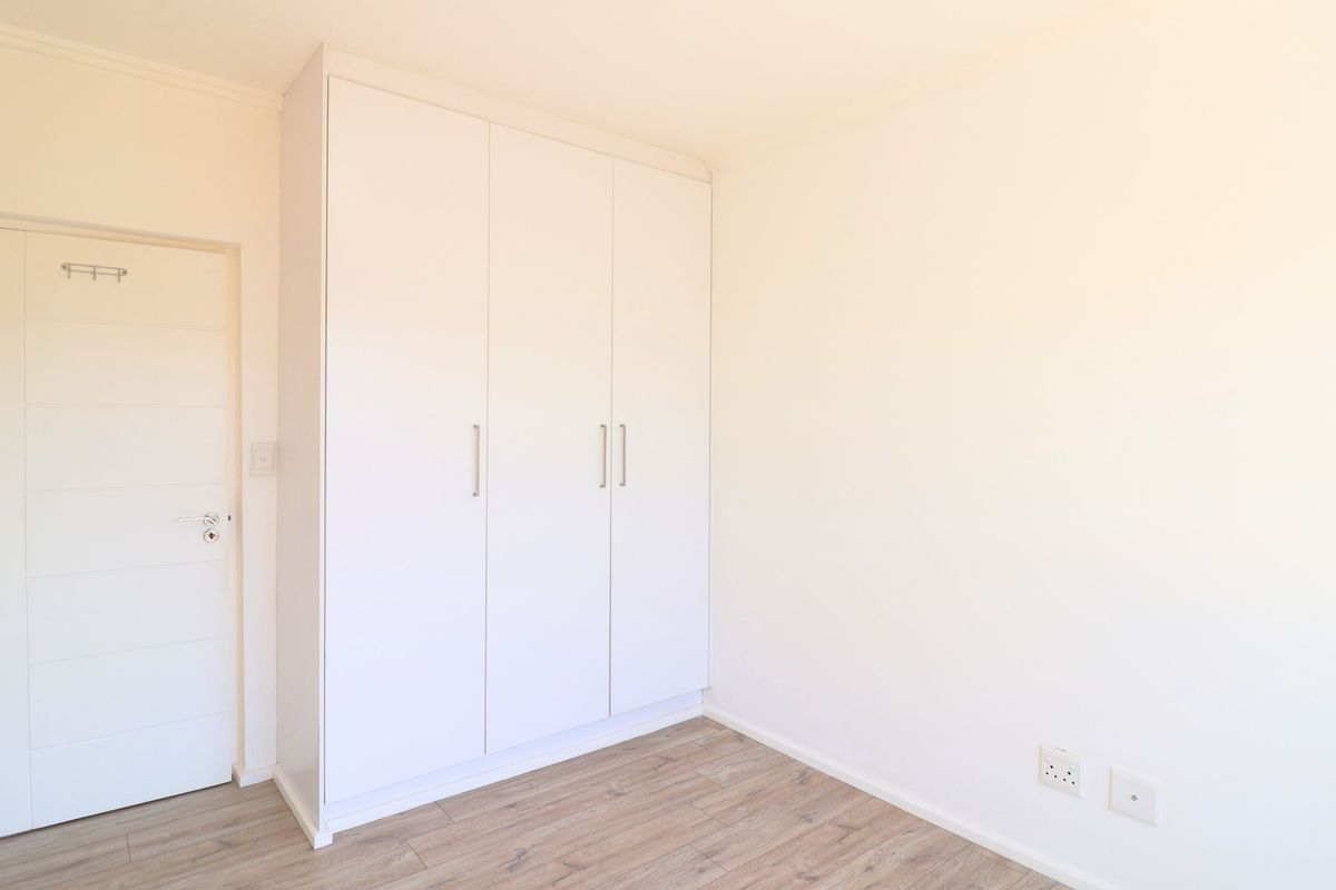 A bright, empty bedroom featuring modern laminate flooring, a clean white built-in wardrobe, and a neutral interior door.