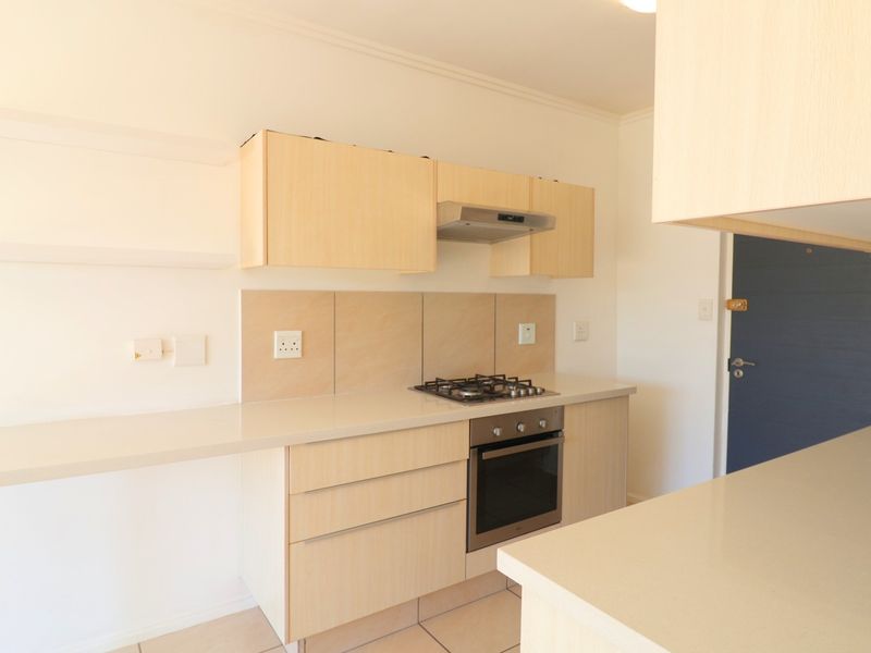 A clean, modern kitchen featuring light wood cabinetry, stone countertops, a built-in gas hob, oven, and extractor fan.