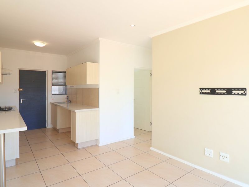 Open-plan living and kitchen area featuring tiled flooring, built-in cabinetry, gas hob, and neutral wall finishes in a well-maintained apartment setting.