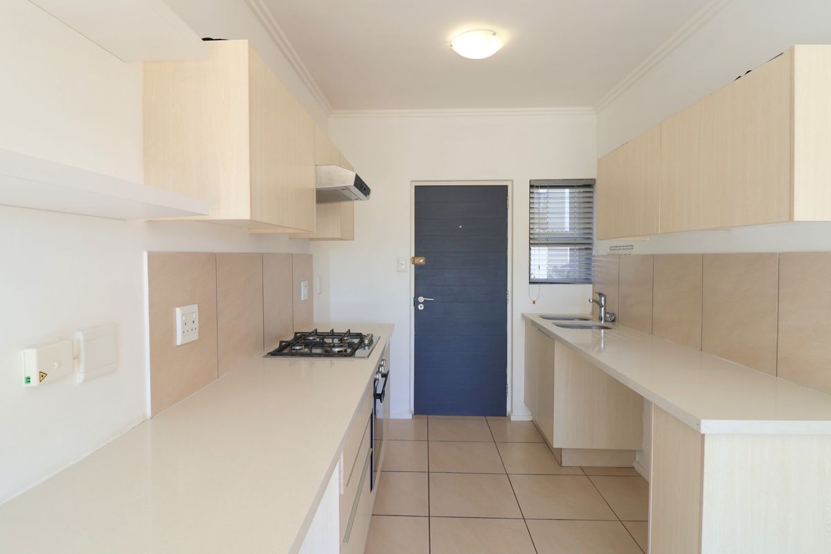 A clean, modern galley-style kitchen featuring light wood cabinetry, gas hob, built-in oven, and neutral tiled finishes throughout.