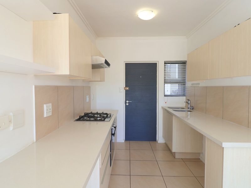 A clean, modern galley-style kitchen featuring light wood cabinetry, gas hob, built-in oven, and neutral tiled finishes throughout.