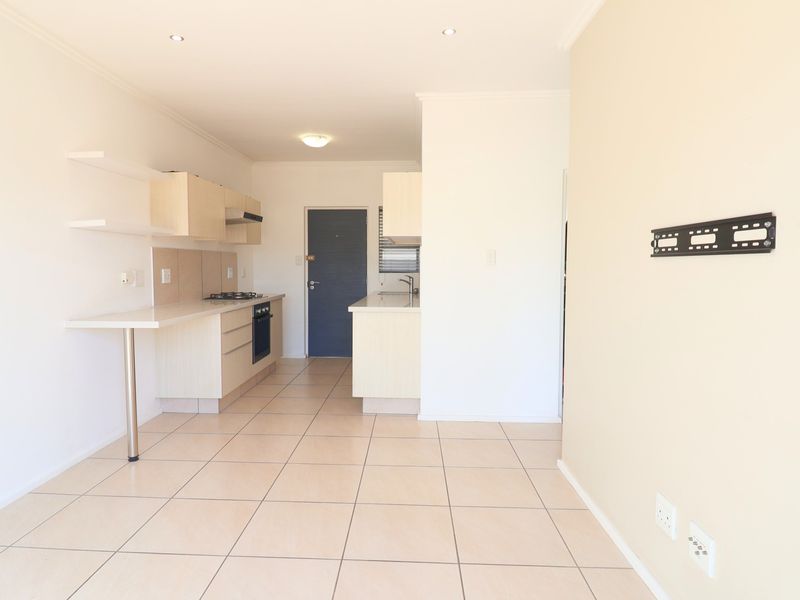Open-plan kitchen and living area featuring tiled flooring, built-in cabinetry, integrated oven and hob, and recessed lighting in a clean, neutral space.