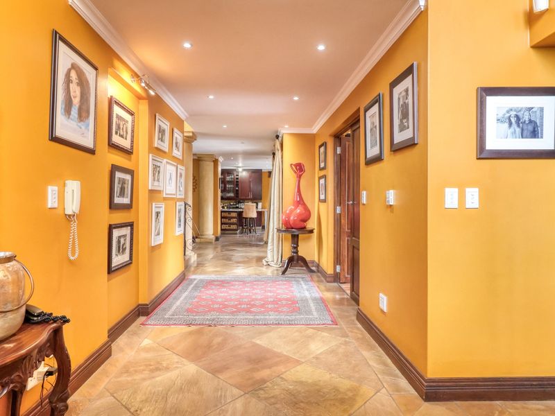 A spacious, well-lit hallway featuring warm-toned walls, crown molding, and tiled flooring, leading towards an open-plan living area.