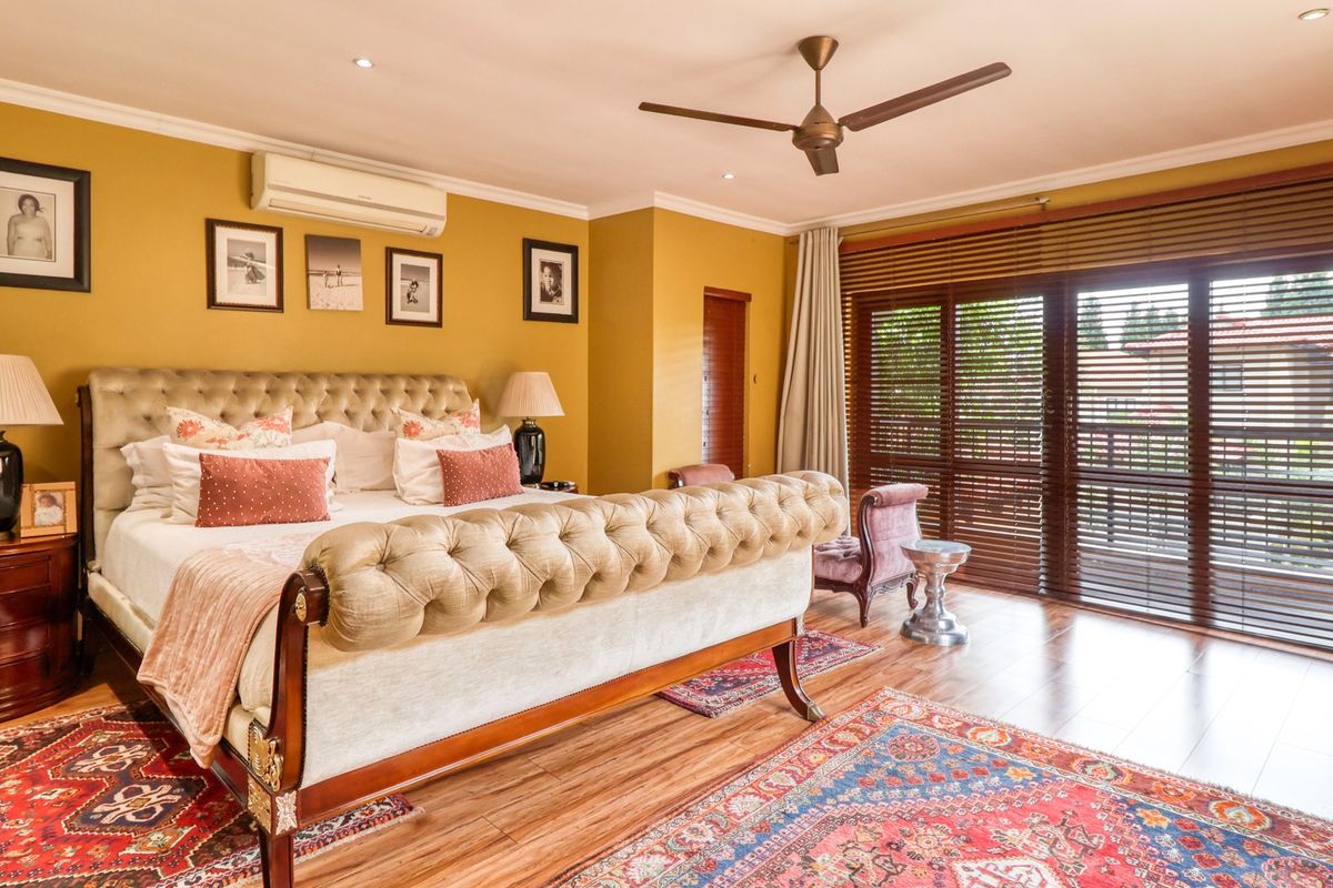 Spacious bedroom featuring timber flooring, recessed downlights, a ceiling fan, and split-system air conditioning, with direct access to an outdoor area through sliding glass doors.