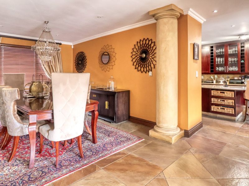 An open-plan dining and kitchen area featuring stone tile flooring, a decorative column, and dark wood cabinetry with a central kitchen island.