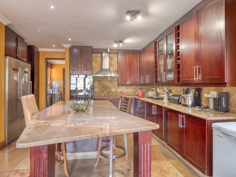 Spacious kitchen featuring dark wood cabinetry, granite countertops, a central island, and a tiled backsplash with integrated stainless steel extractor fan.